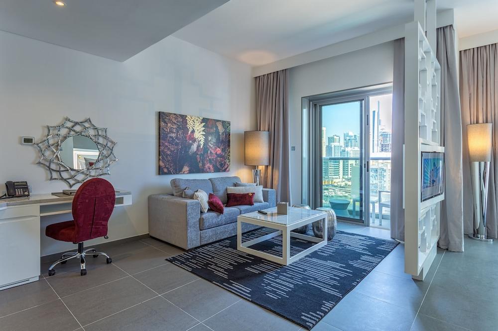 The First Collection Dubai Marina Hotel Exterior photo The photo shows a modern living space designed with a contemporary aesthetic. It features a comfortable gray sofa with colorful cushions, a stylish glass coffee table, and a dark patterned rug on the floor. There is a small desk with a red chair posi